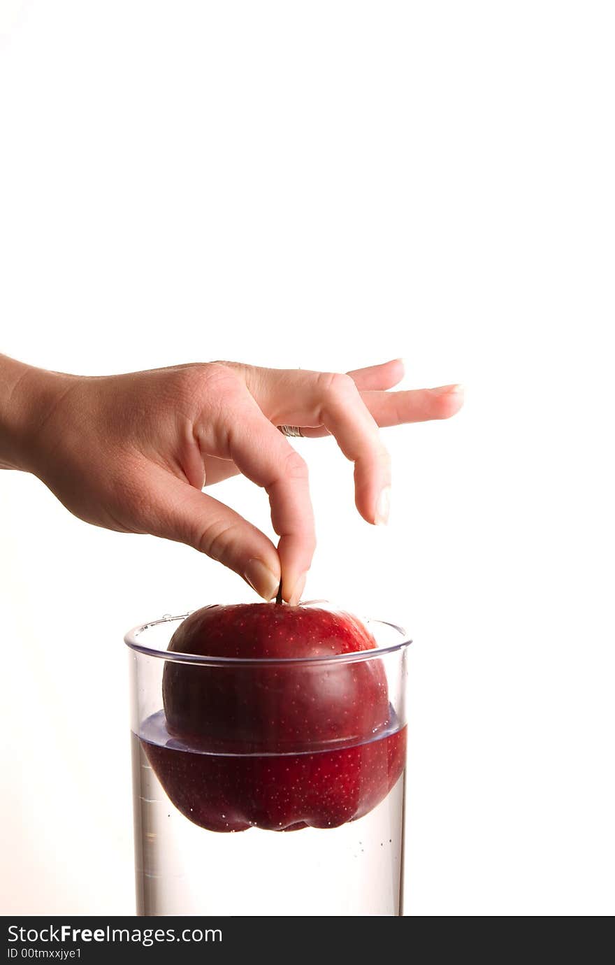 A hand dropping an apple in glass water. A hand dropping an apple in glass water