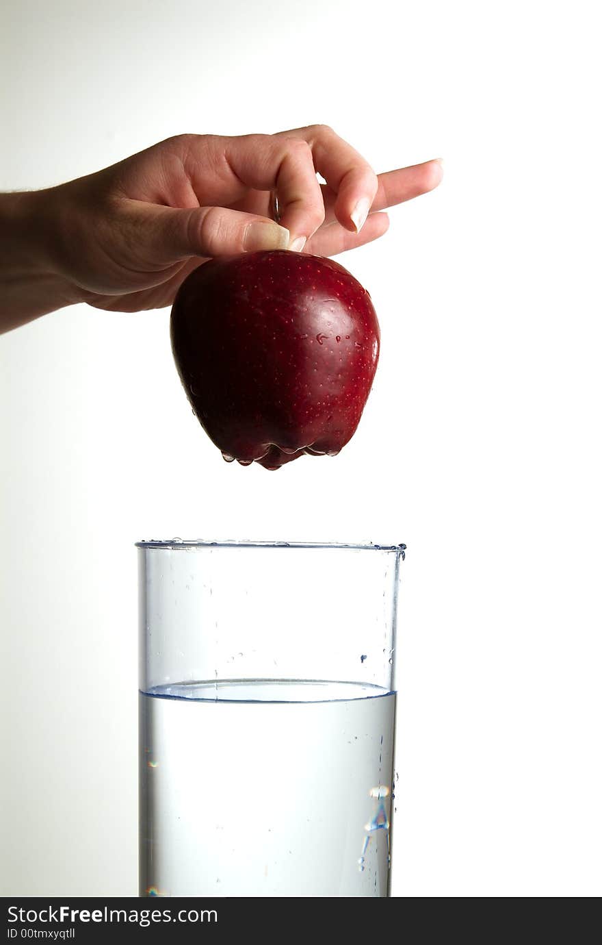 A hand dropping an apple in glass water. A hand dropping an apple in glass water