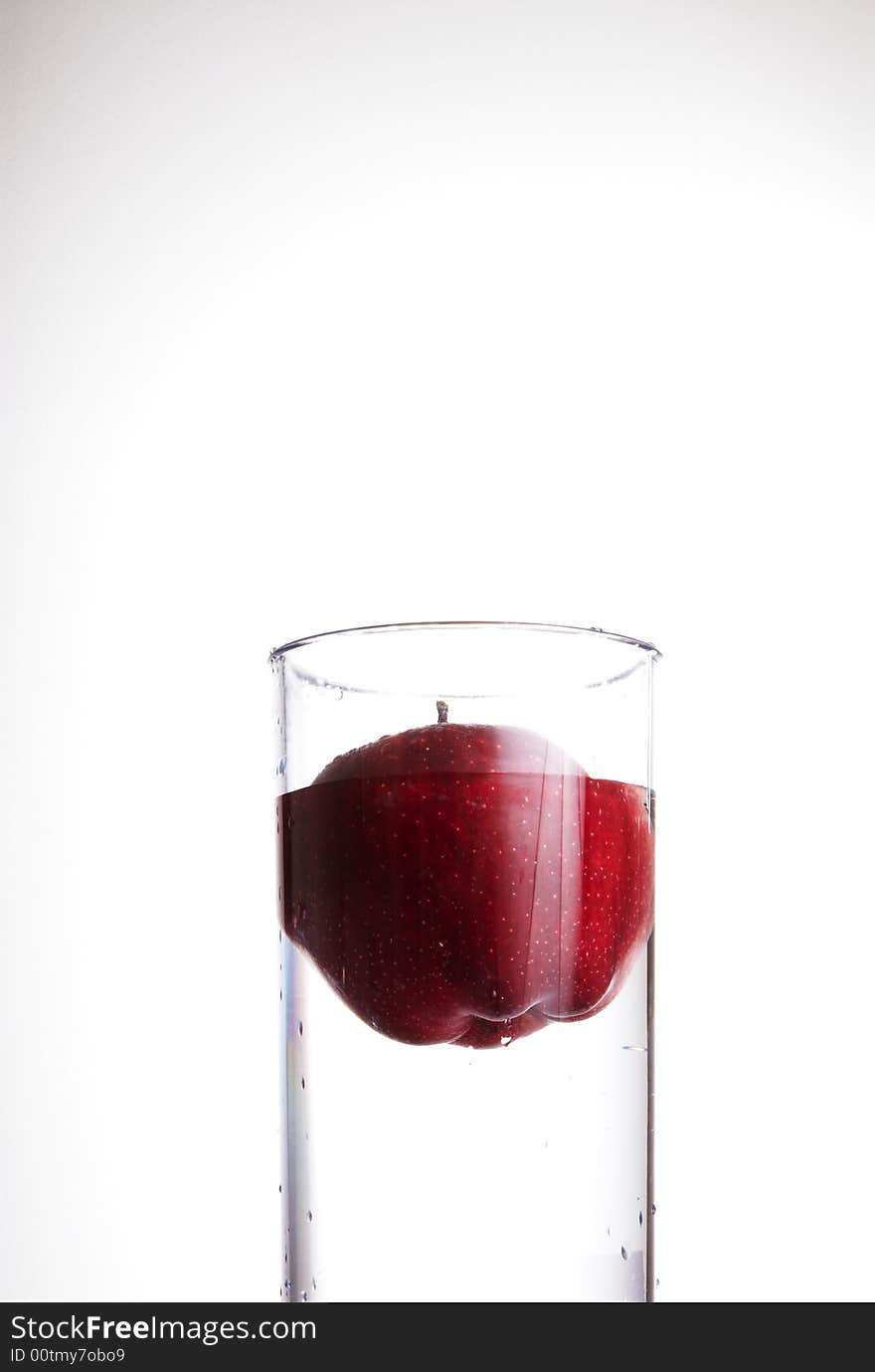 Glass of water and red apple floating in it.