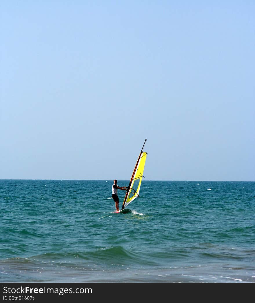 A yellow windsurfer and sailboad on the sea. A yellow windsurfer and sailboad on the sea