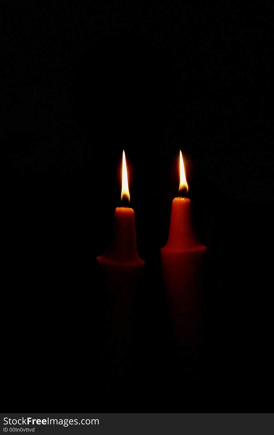 Two candles light in darkness