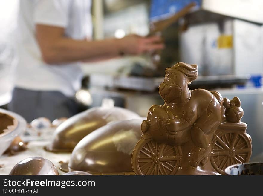 Making chocolate bunny in a bakery. close-up of bunny.  Baker on background working..