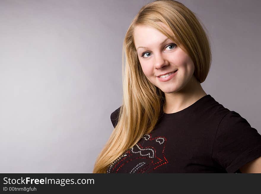 The smiling blonde on a grey background in studio.