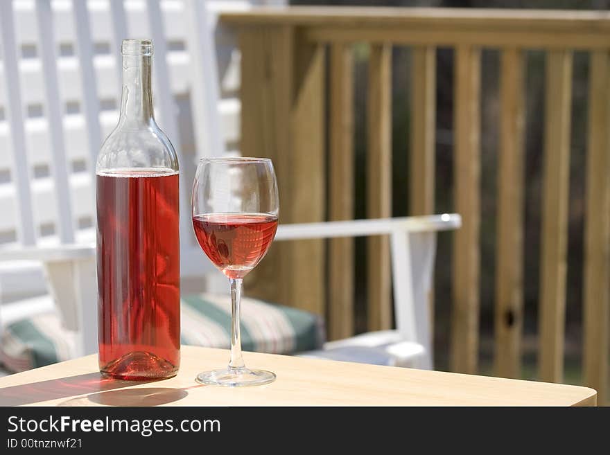 Wine and glass on deck with white chair and deck railing in background