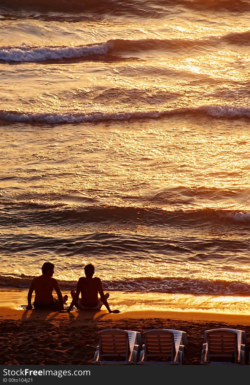 Photo of beautiful sunset, two friends seating on the beach