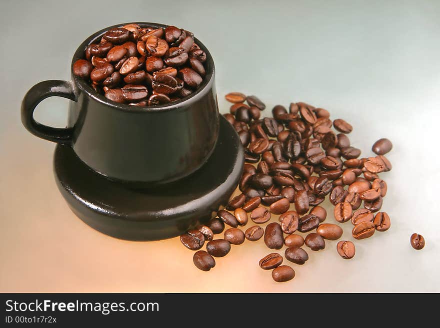 Coffee beans of two kind in a little brown cup and saucer on color background from glass. Coffee beans of two kind in a little brown cup and saucer on color background from glass