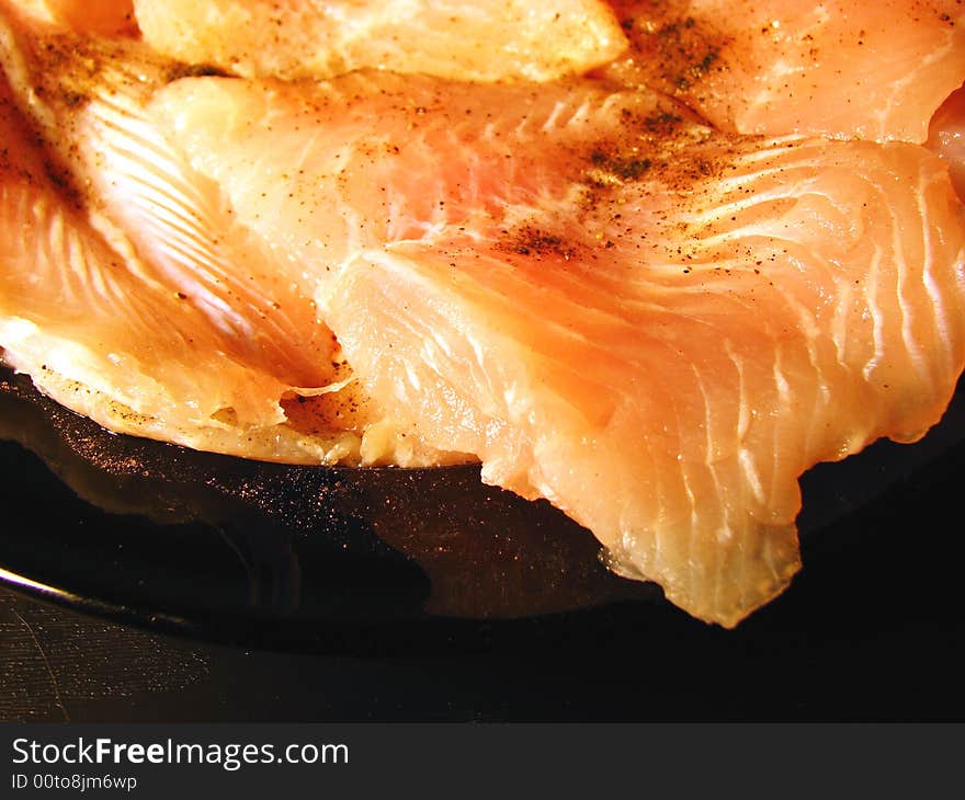 Defrosted fish closeup on black plate with black pepper ready to fry.