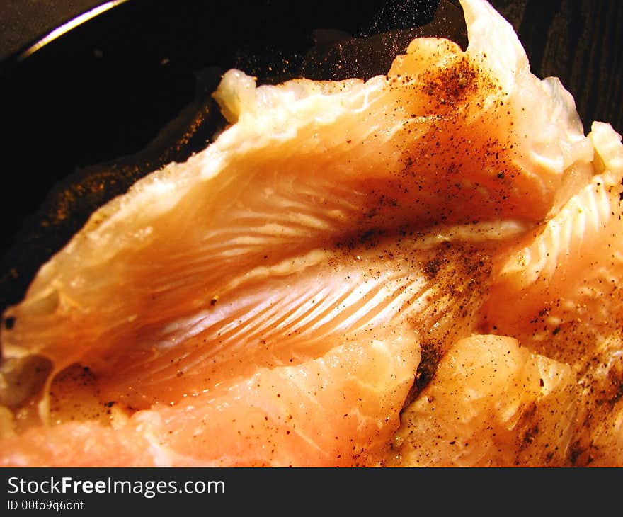 Defrosted raw fish on black plate with black pepper ready to fry in vertical view.