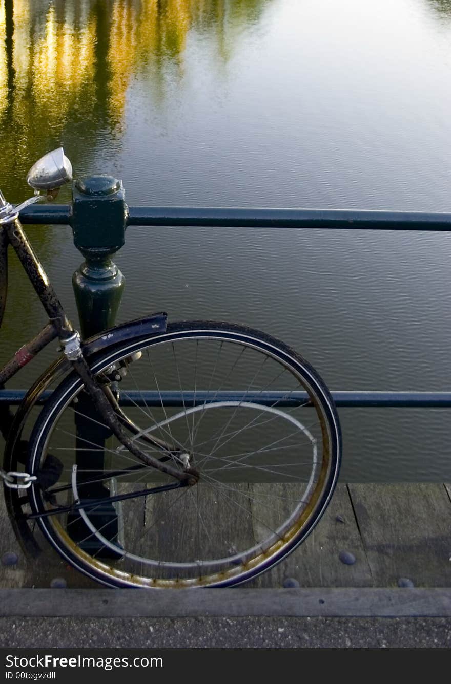 Detail of a bicycle wheel against a railing by a canal