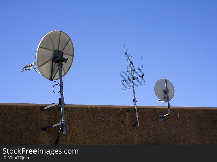 A television aerial and two satellite dishes bolted to a wall. A television aerial and two satellite dishes bolted to a wall.