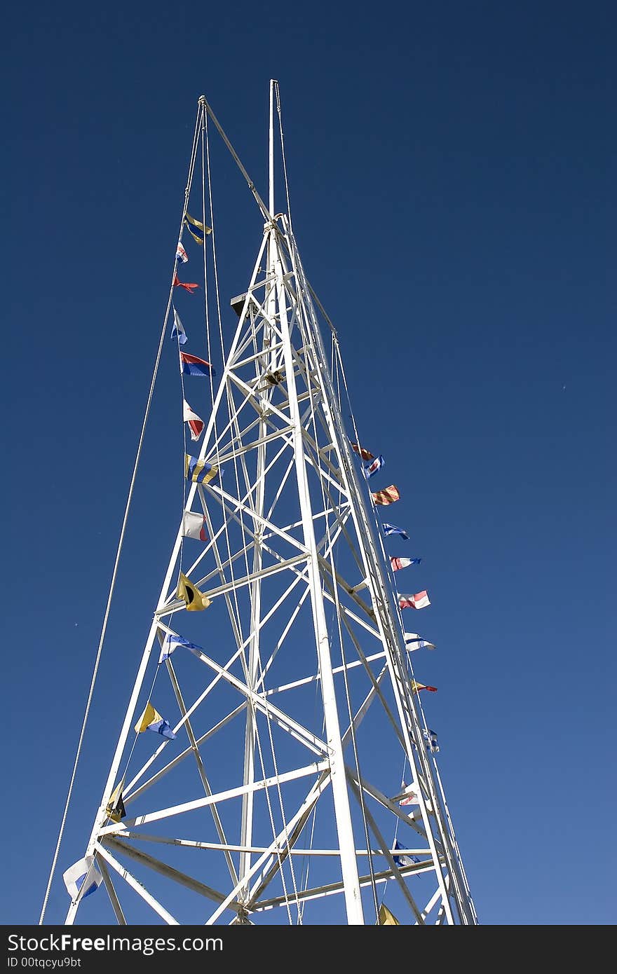 A white tower with nautical flags on ropes against a blue sky. A white tower with nautical flags on ropes against a blue sky