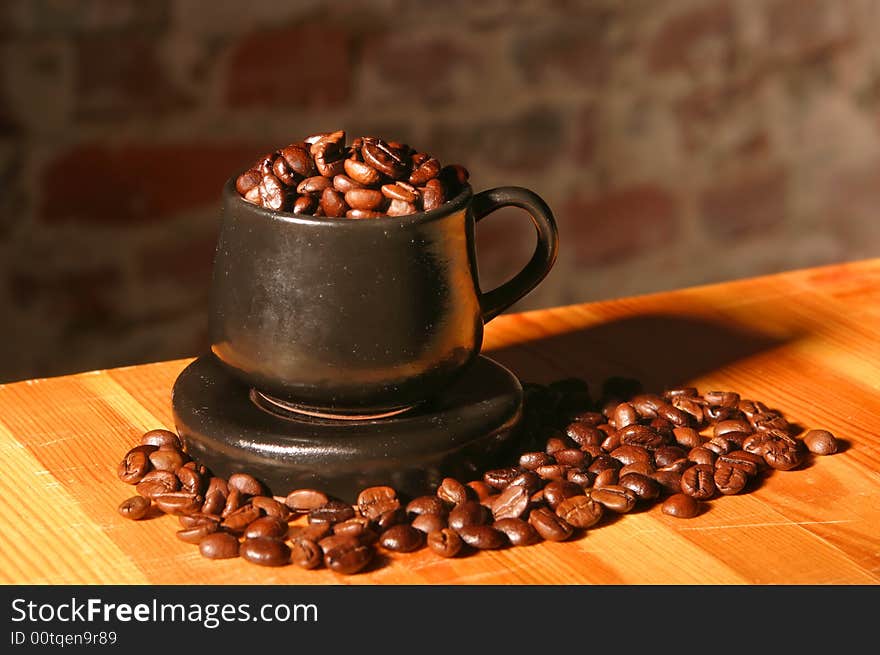 Little brown cup and spilled out coffee beans on soft focus background on wood table. Little brown cup and spilled out coffee beans on soft focus background on wood table