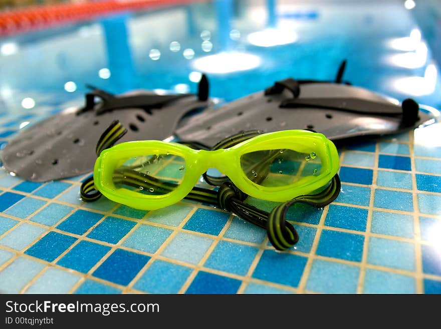 Glasses and paddle for swim lay on the coast of swimming pool. Glasses and paddle for swim lay on the coast of swimming pool