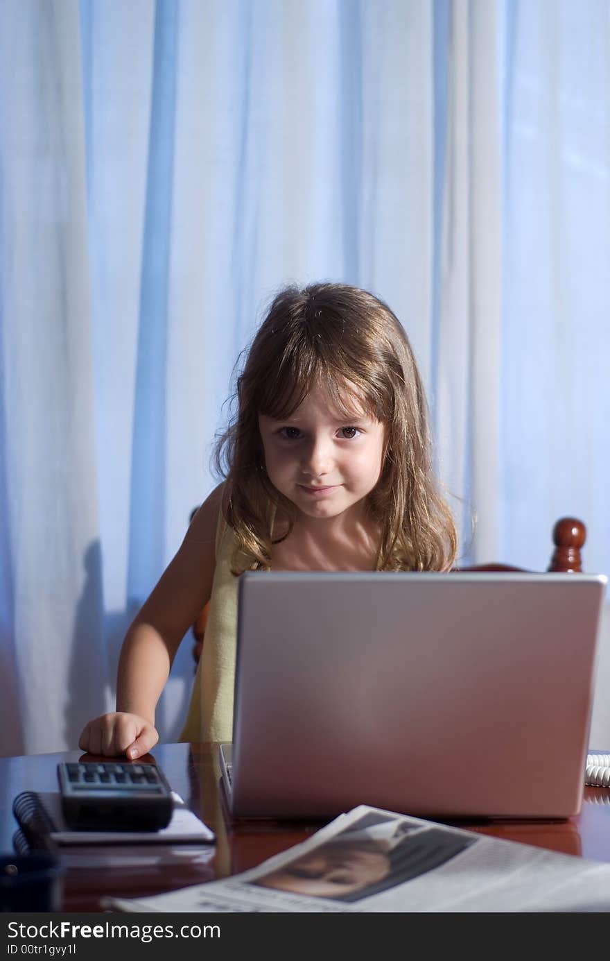 Little girl behind a laptop in a home office. Little girl behind a laptop in a home office