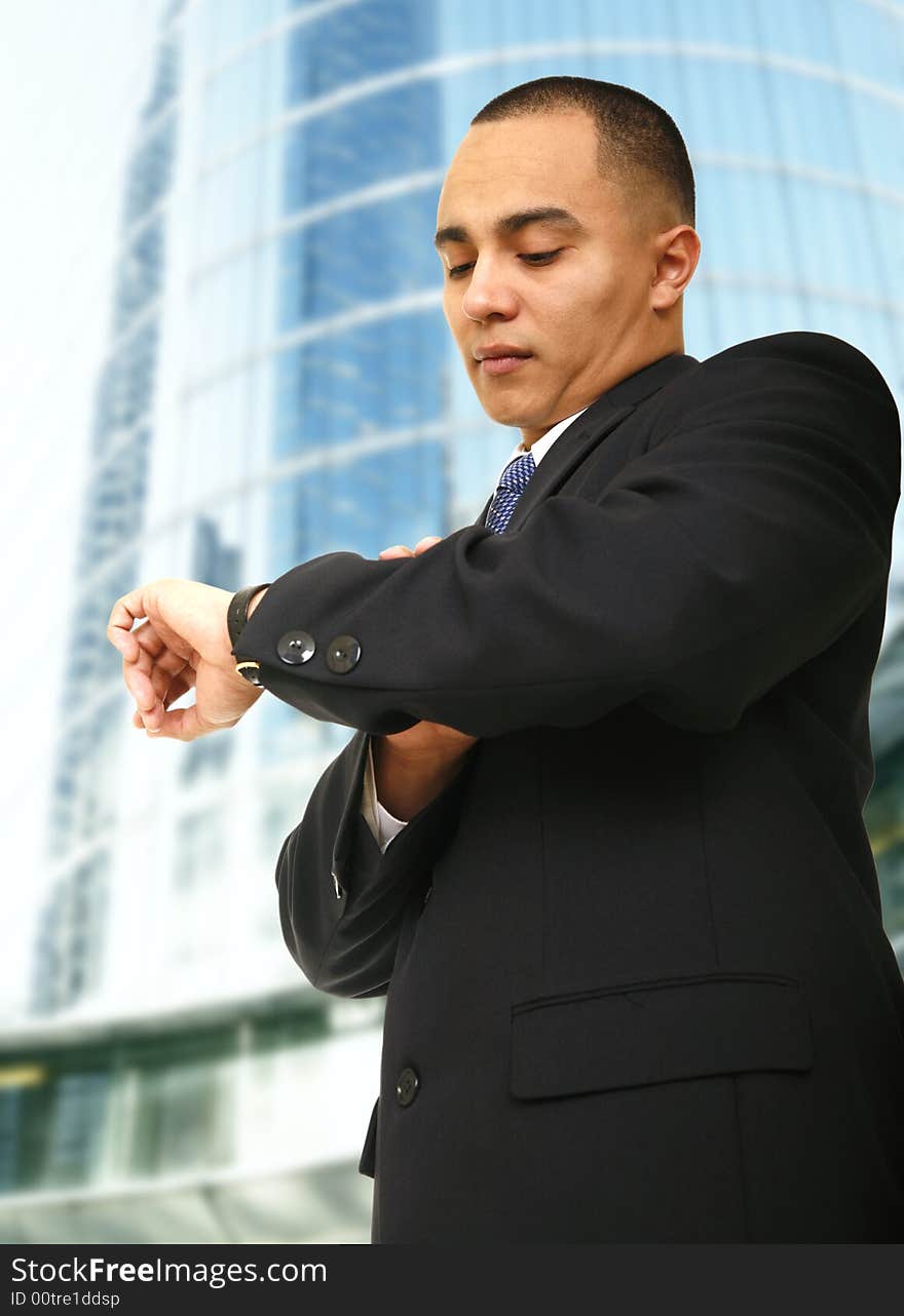 Close up of a man checking out his watch outdoor in front of tall and modern business building. Close up of a man checking out his watch outdoor in front of tall and modern business building