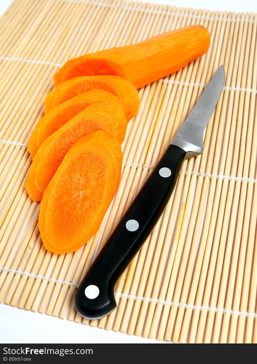 Carrot sliced , knife behind the carrot, and a bamboo carpet background.