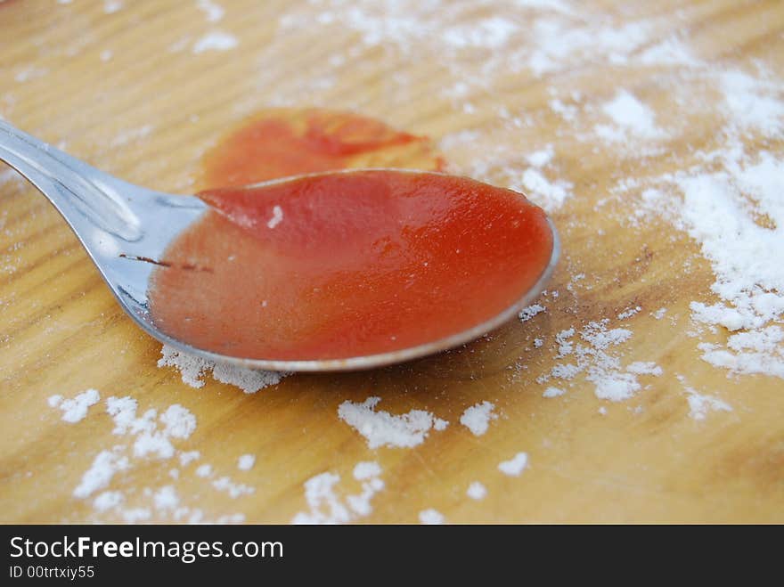 A spoon with red tomato sauce and flour on a wooden table