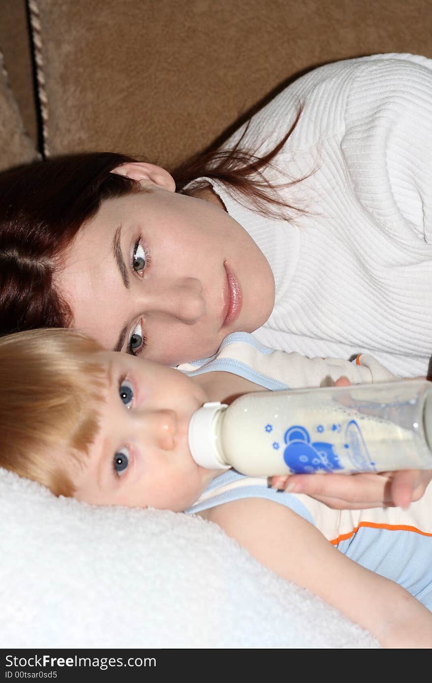 Young mum feeds the small beautiful son laying on a sofa. Young mum feeds the small beautiful son laying on a sofa