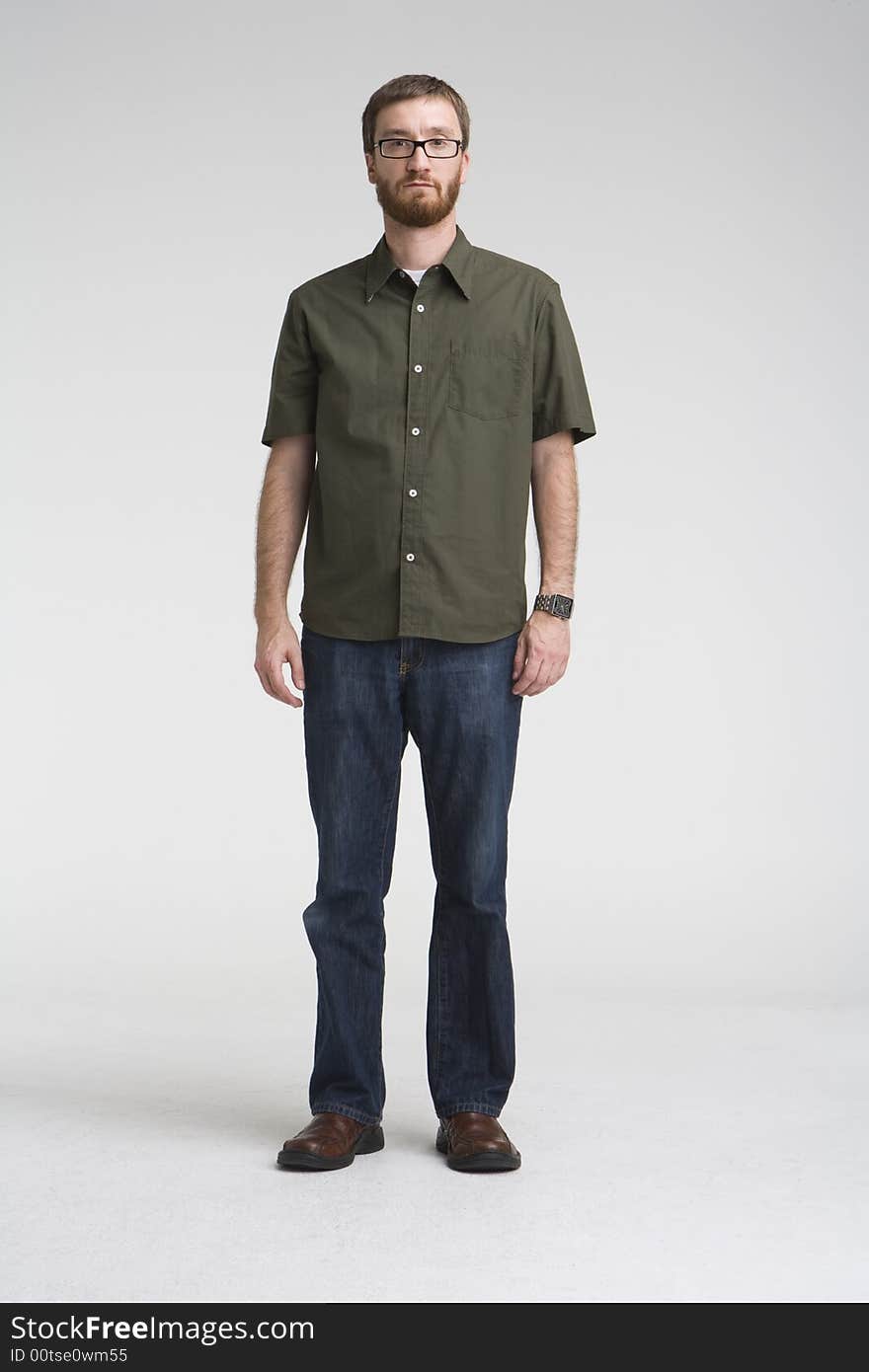 Full length image of a man with beard wearing a green shirt and denim jeans stands in a gray photo studio. Full length image of a man with beard wearing a green shirt and denim jeans stands in a gray photo studio.