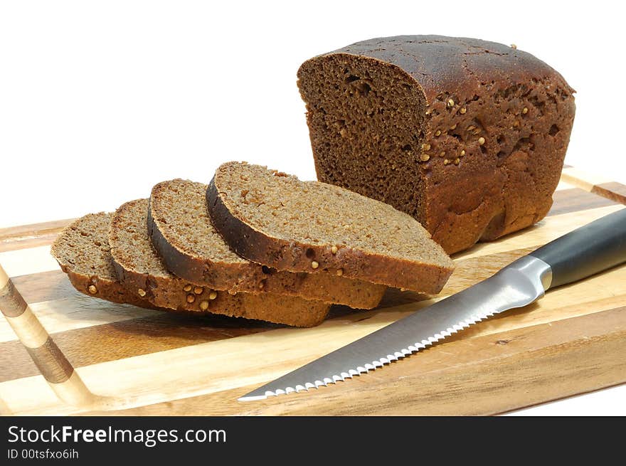 Loaf of sliced grain bread on wood bread board with knife isolated on white