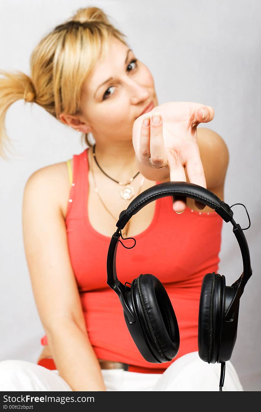 Sitting woman clothed in T-shirt and trousers holding headphones. Focus on headphones.