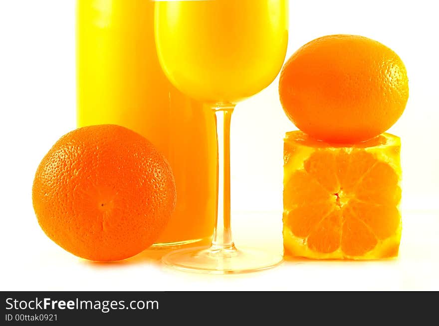 Partial view at the brightly lit oranges, bottle and glass with orange juice. Partial view at the brightly lit oranges, bottle and glass with orange juice