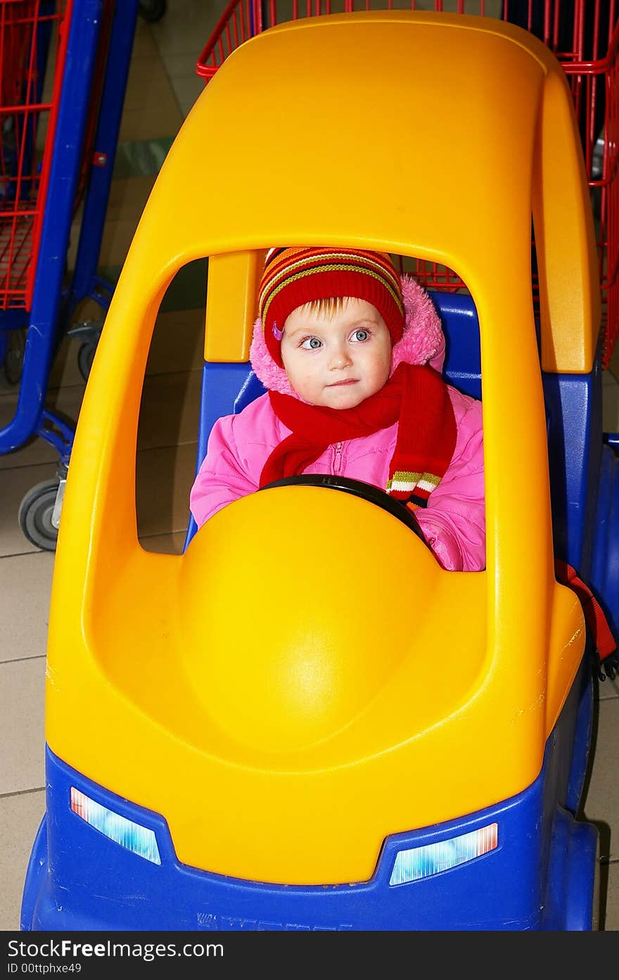 Little girl in the carriage in the form of the machine in a supermarket. Little girl in the carriage in the form of the machine in a supermarket