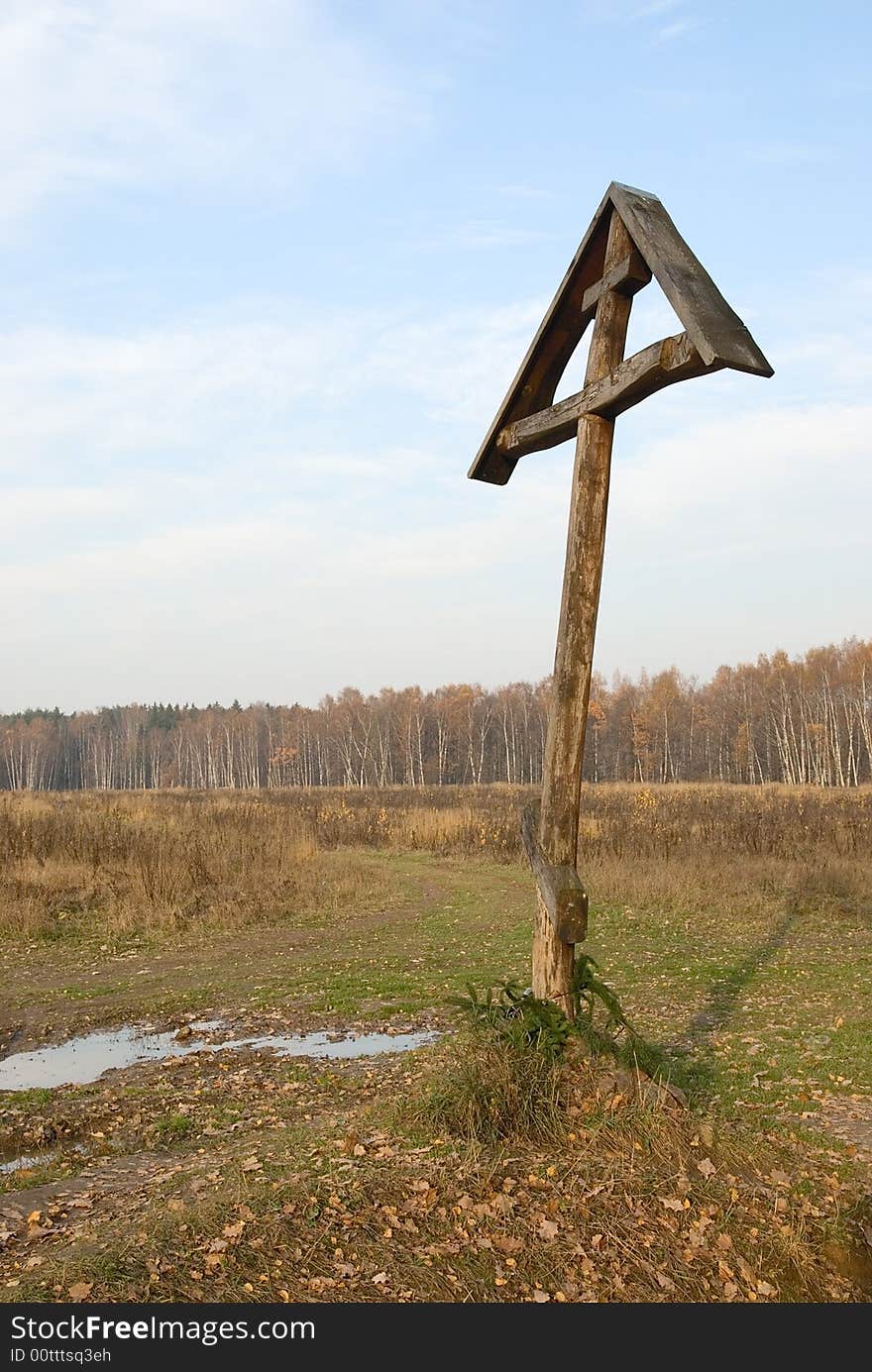 Wooden Christian cross near the path in the field