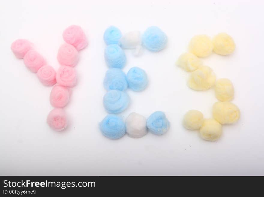 Word yes with blue, yellow and pink hygienic cotton balls isolated on a white background. Word yes with blue, yellow and pink hygienic cotton balls isolated on a white background