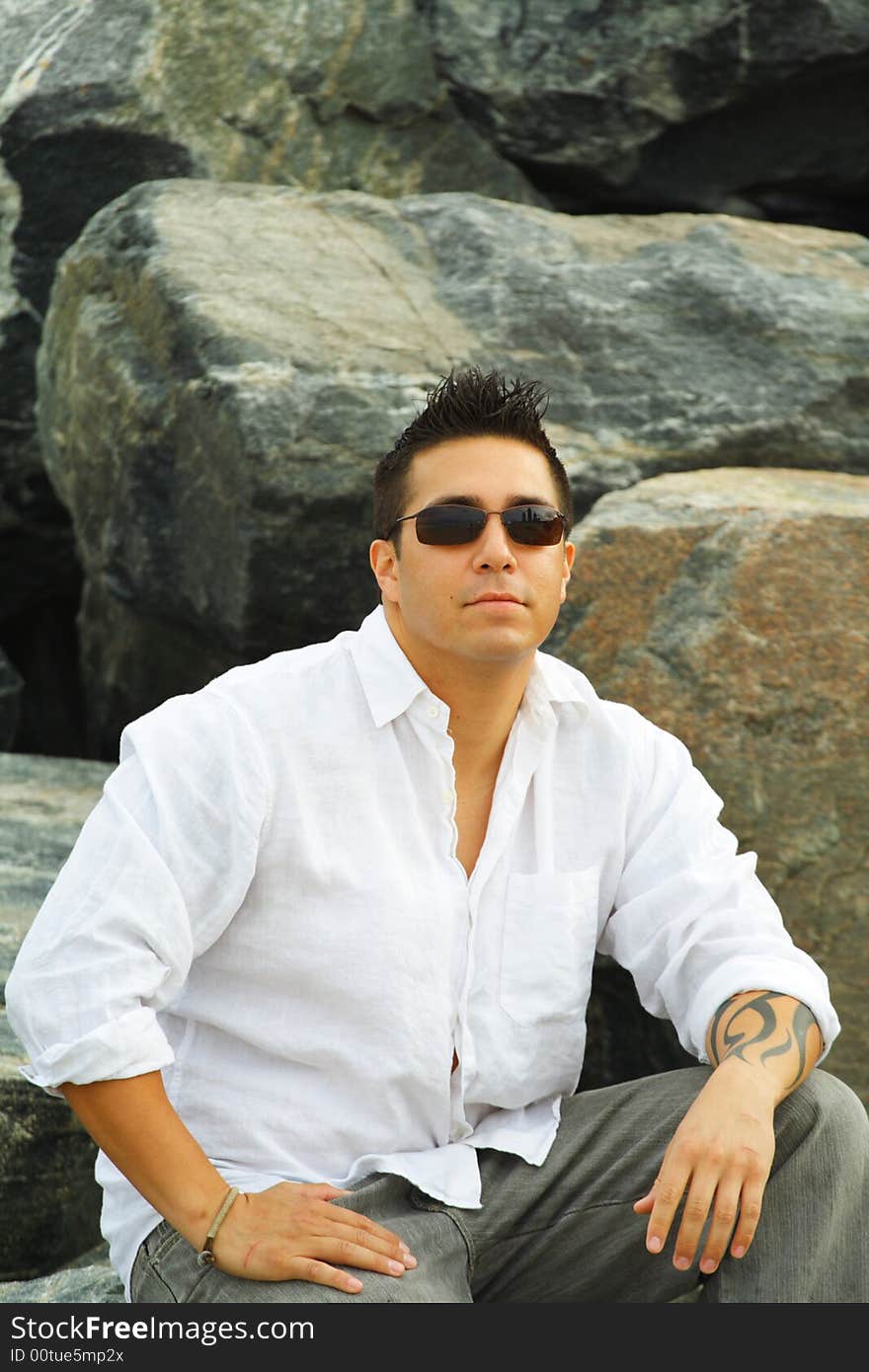 Man sitting on a rock with rocks as a background and wearing sunglasses. Man sitting on a rock with rocks as a background and wearing sunglasses