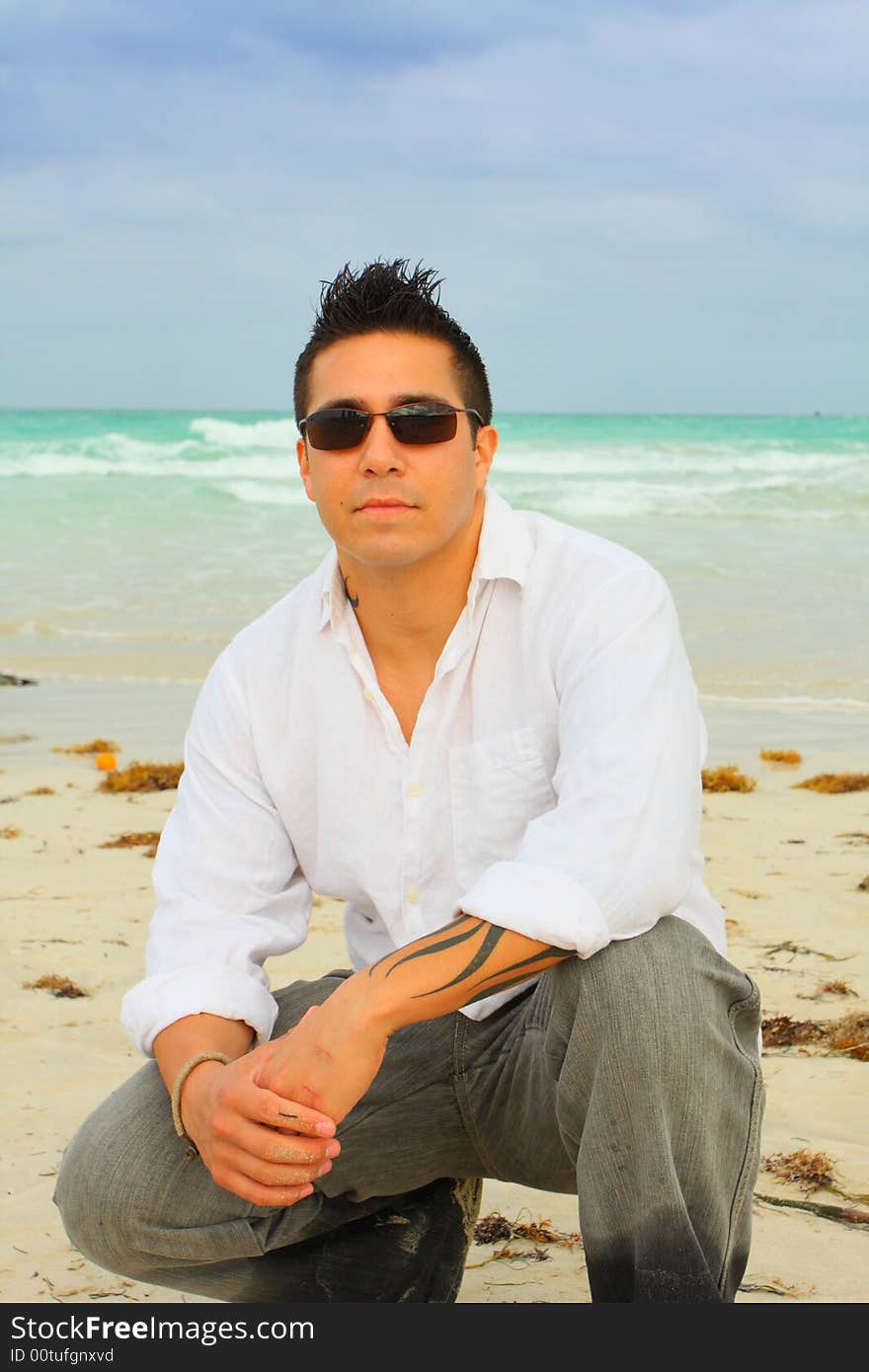 Man squatting down on the sand with the ocean behind him. Man squatting down on the sand with the ocean behind him.