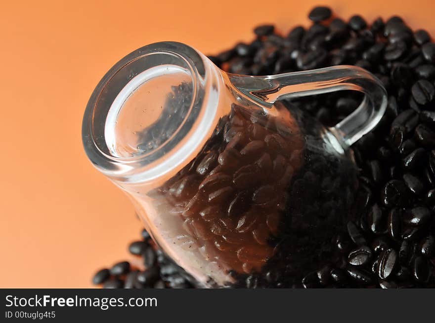 Transparent glass coffe cup up side down with coffe beans isolated on orange. Transparent glass coffe cup up side down with coffe beans isolated on orange