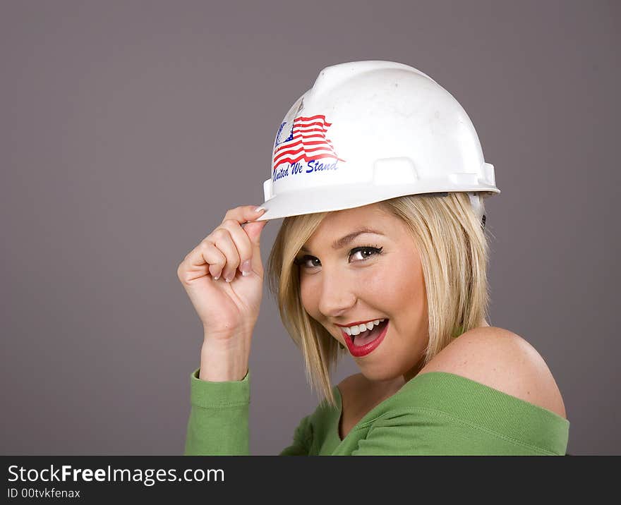 A blonde in a green blouse tipping a hard hat to the camera. A blonde in a green blouse tipping a hard hat to the camera