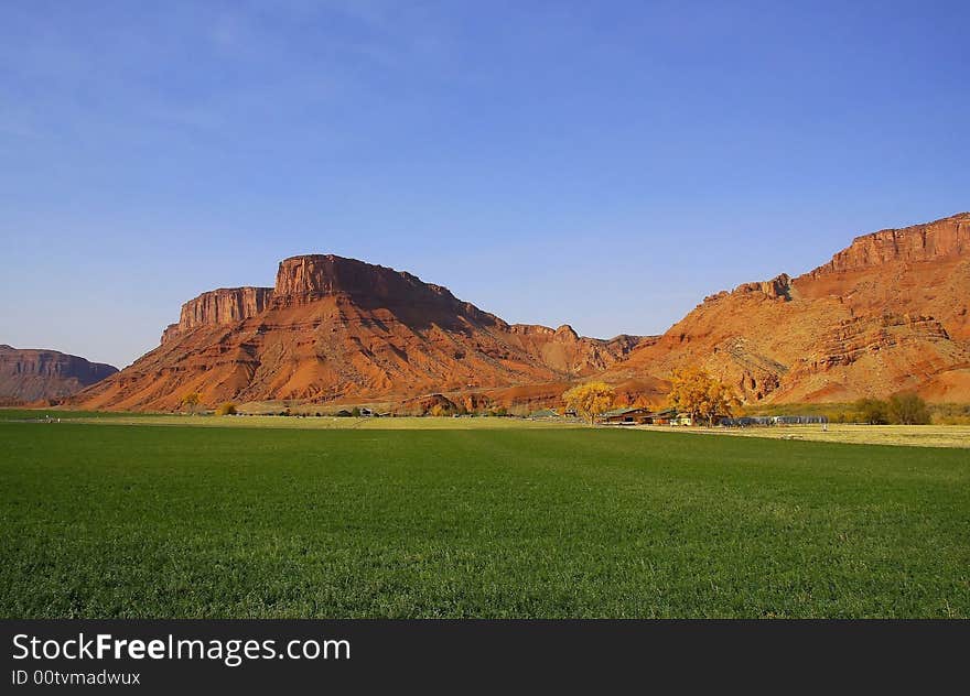 View of a farm in the desert with hay in the foreground and a red rock mountain in the background with blue sky�s and puffy clouds. View of a farm in the desert with hay in the foreground and a red rock mountain in the background with blue sky�s and puffy clouds