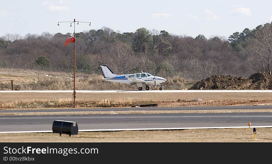 A small private blue and white plane on a runway at a regional airport. A small private blue and white plane on a runway at a regional airport