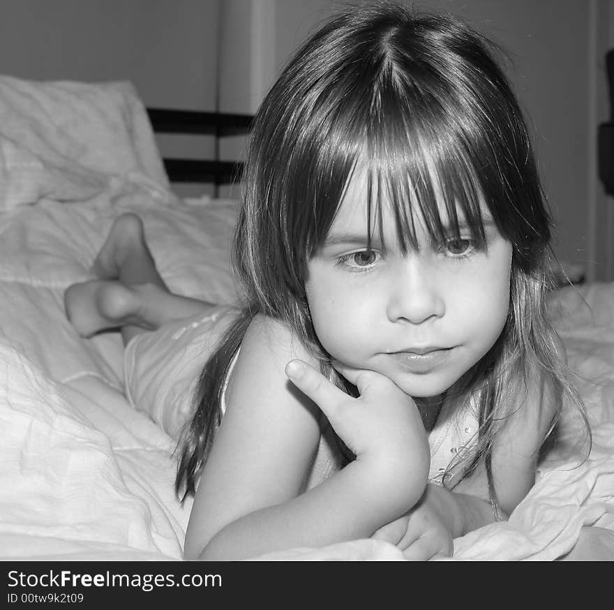 Sad little girl laying on a bed with a thoughtful expression. Sad little girl laying on a bed with a thoughtful expression.