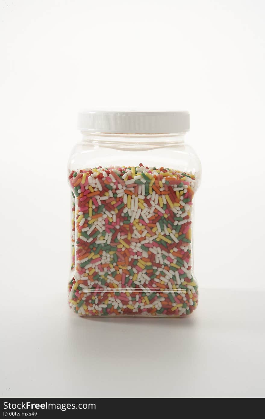 A plastic jar of sprinkles on a white table lit darkly. A plastic jar of sprinkles on a white table lit darkly.