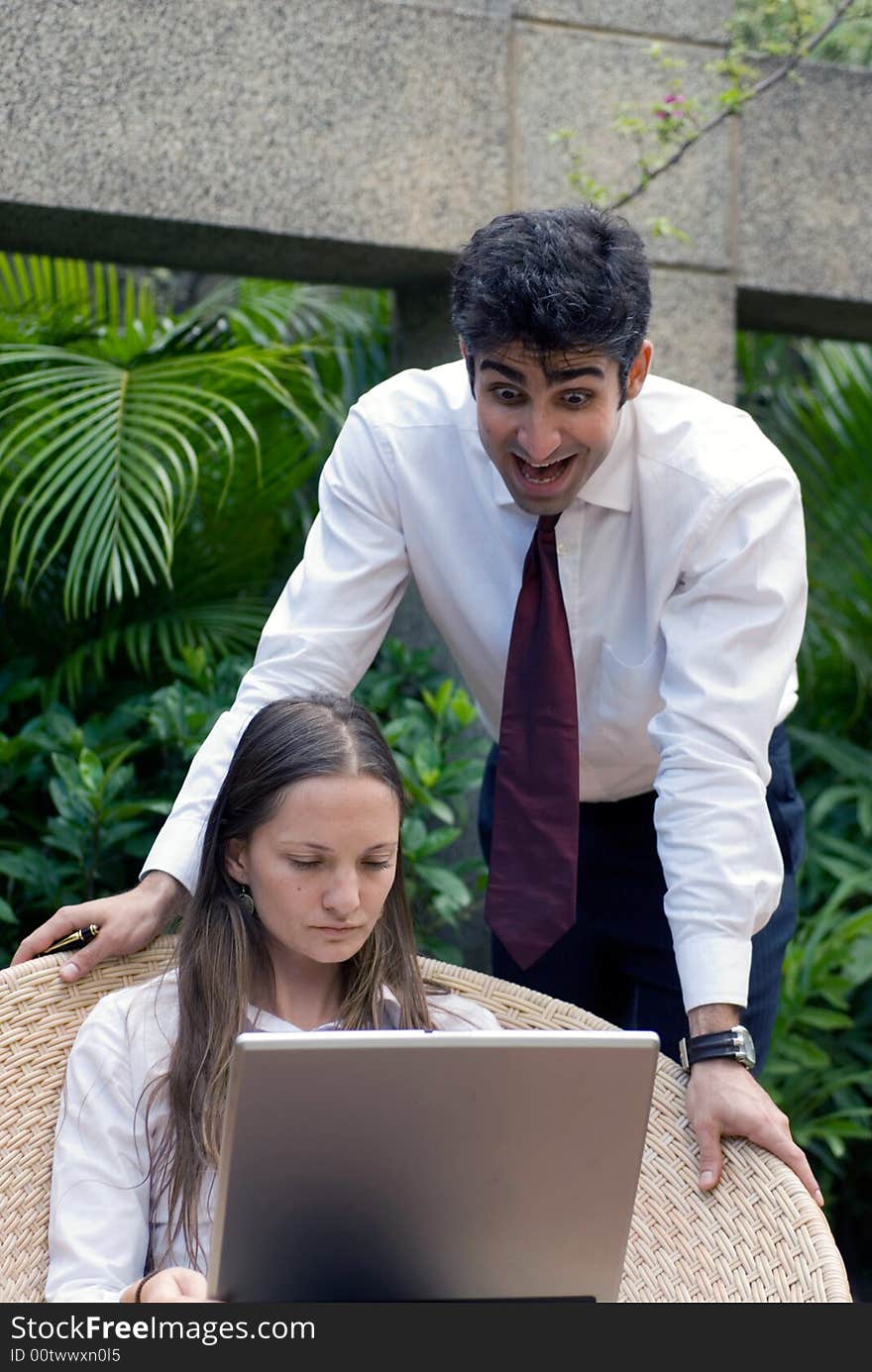 Male colleague surprised by what he is reading on his female colleague's laptop screen. Male colleague surprised by what he is reading on his female colleague's laptop screen