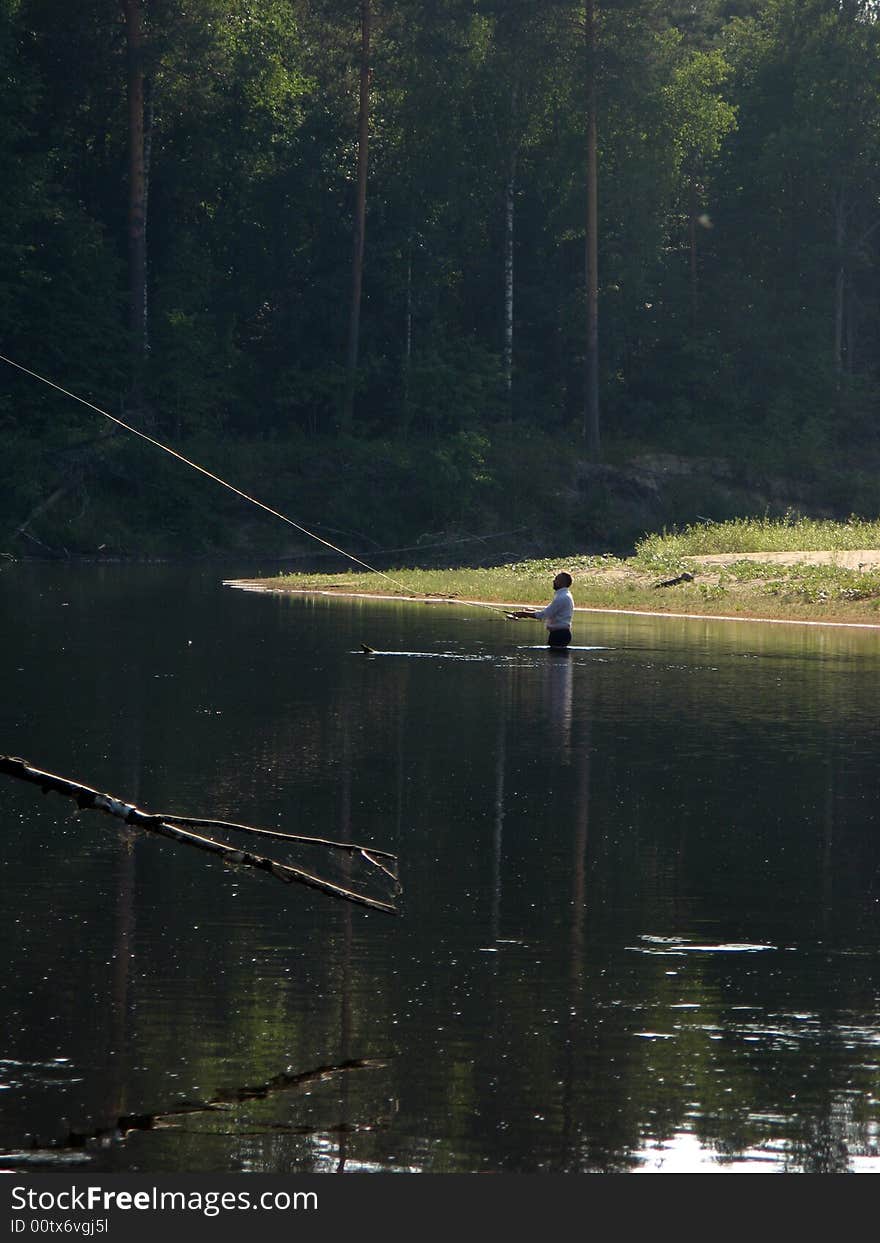 The person fishs around fishes in the wood river on a background of trees. The person fishs around fishes in the wood river on a background of trees