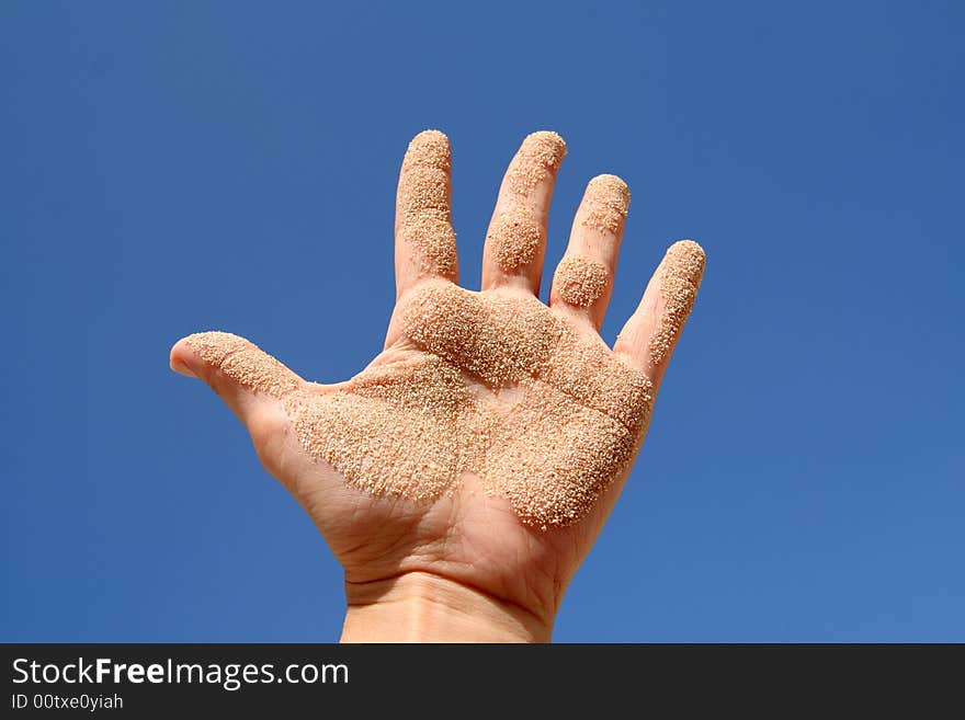 Woman's hand with sand on blue sky. Woman's hand with sand on blue sky