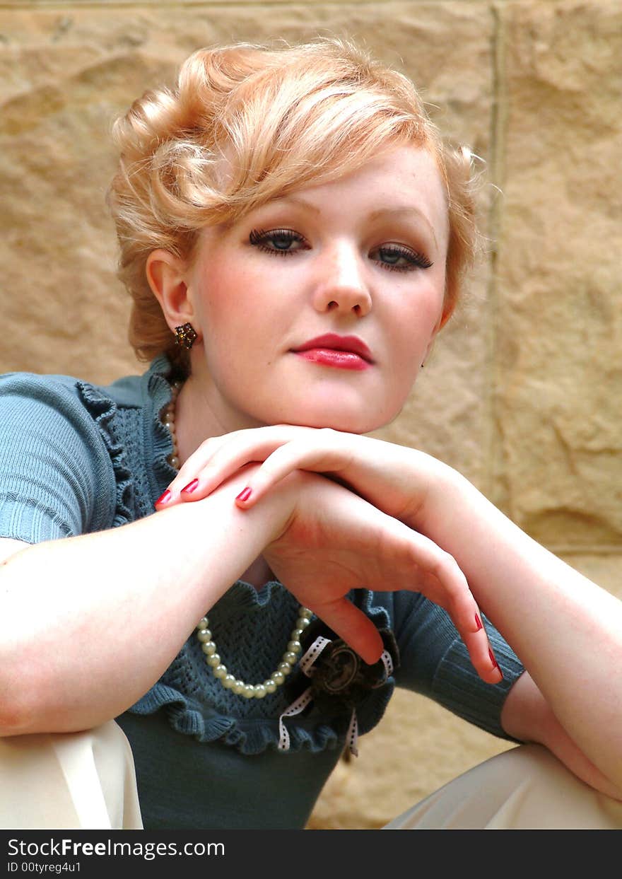 Closeup of young blond woman leaning on hands in front of stone wall, looking at camera