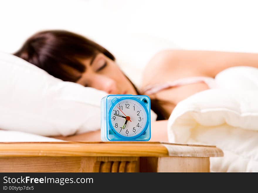 Brunette in bed with an alarmclock at the front. Brunette in bed with an alarmclock at the front