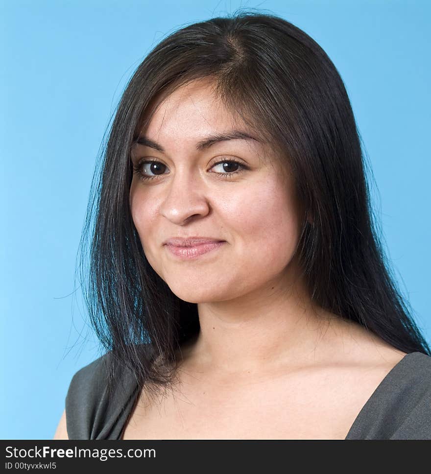 A portrait of a young, naturally beautiful Hispanic woman taken against a blue background. A portrait of a young, naturally beautiful Hispanic woman taken against a blue background.