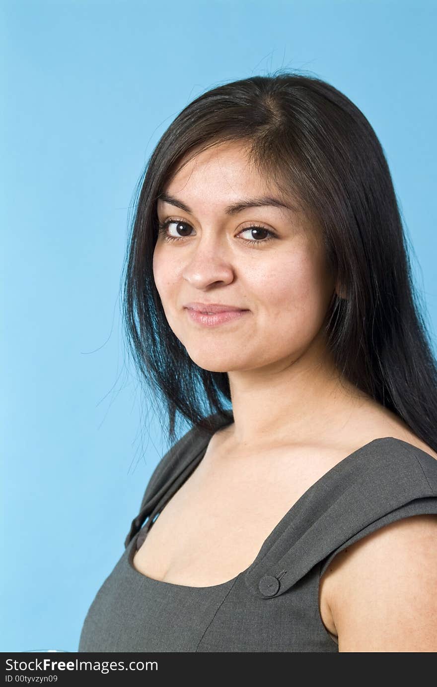 A portrait of a young, naturally beautiful Hispanic woman taken against a blue background. A portrait of a young, naturally beautiful Hispanic woman taken against a blue background.