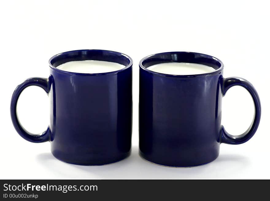 Two dark-blue cups with the milk against the white background