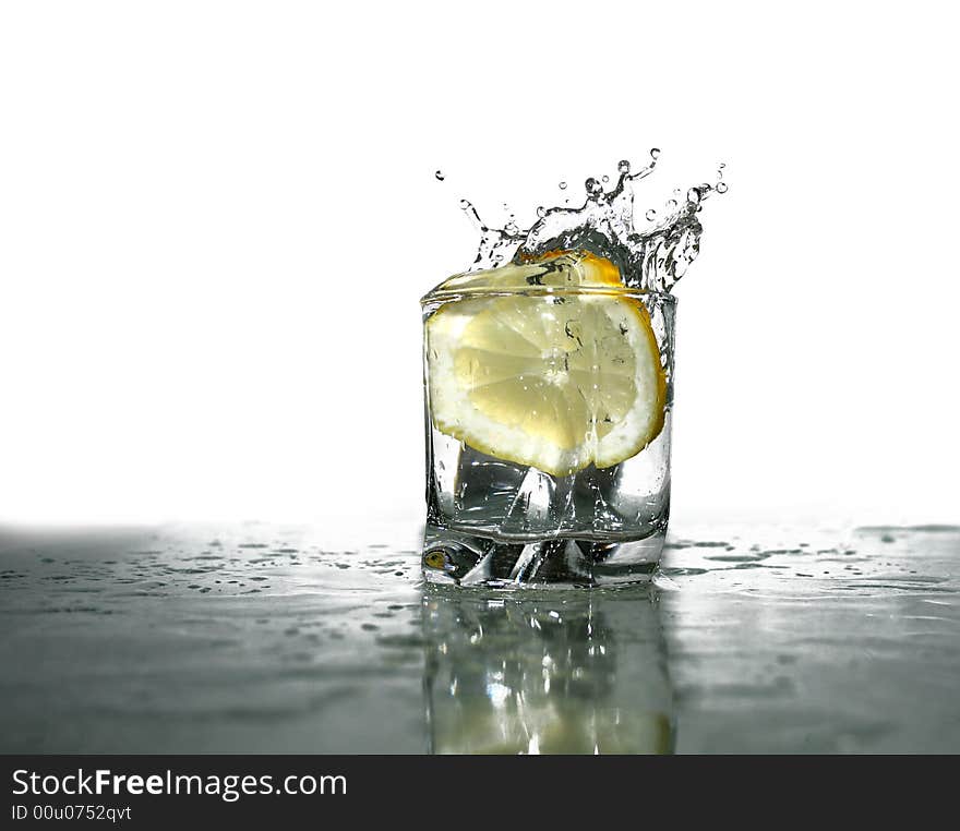 Glass of cold clear splashing water with falling lemon's slice on light-blue background. Glass of cold clear splashing water with falling lemon's slice on light-blue background