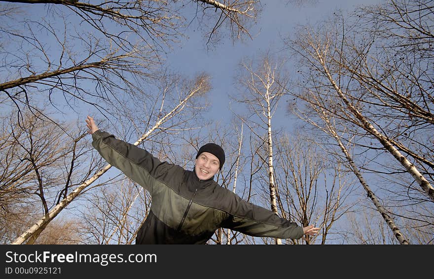 Young emotional guy has widely placed hands on background of trees. Young emotional guy has widely placed hands on background of trees