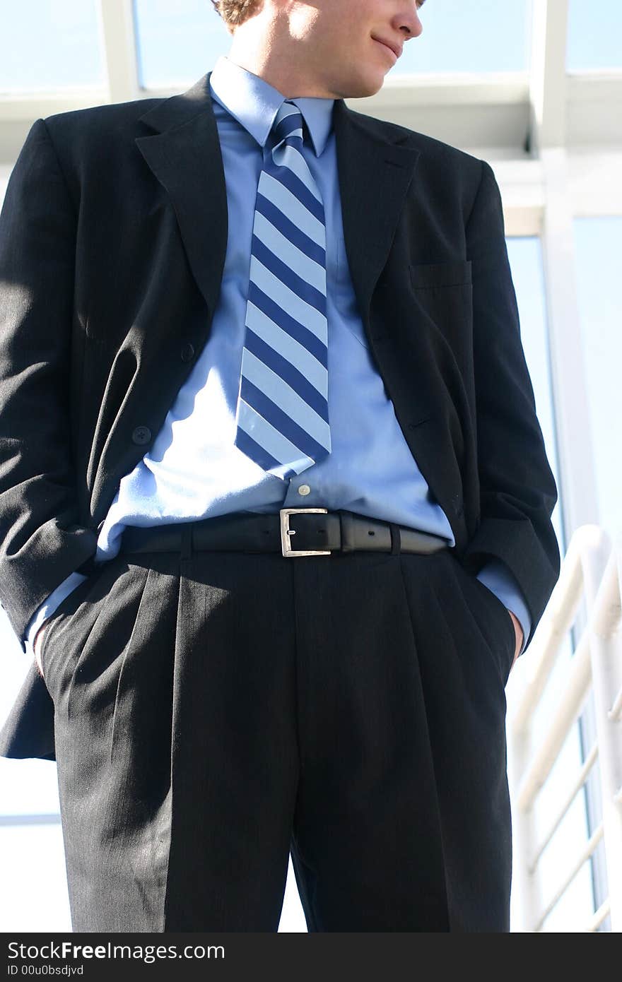 Close-up of single white businessman wearing suit with hands in pockets looking down smiling. Close-up of single white businessman wearing suit with hands in pockets looking down smiling