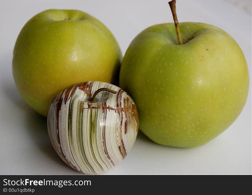 Two green granny smith apples one with a stalk and a polished hand carved white onyx apple streaked with green and brown with a brass stalk. Two green granny smith apples one with a stalk and a polished hand carved white onyx apple streaked with green and brown with a brass stalk