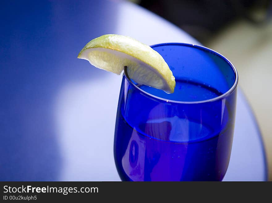 A lemon slice on a blue crystal water glass against a blue table. A lemon slice on a blue crystal water glass against a blue table